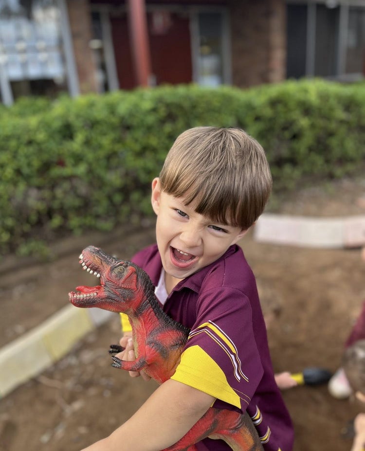 Happy boy student holding dinosaur in dirt pit